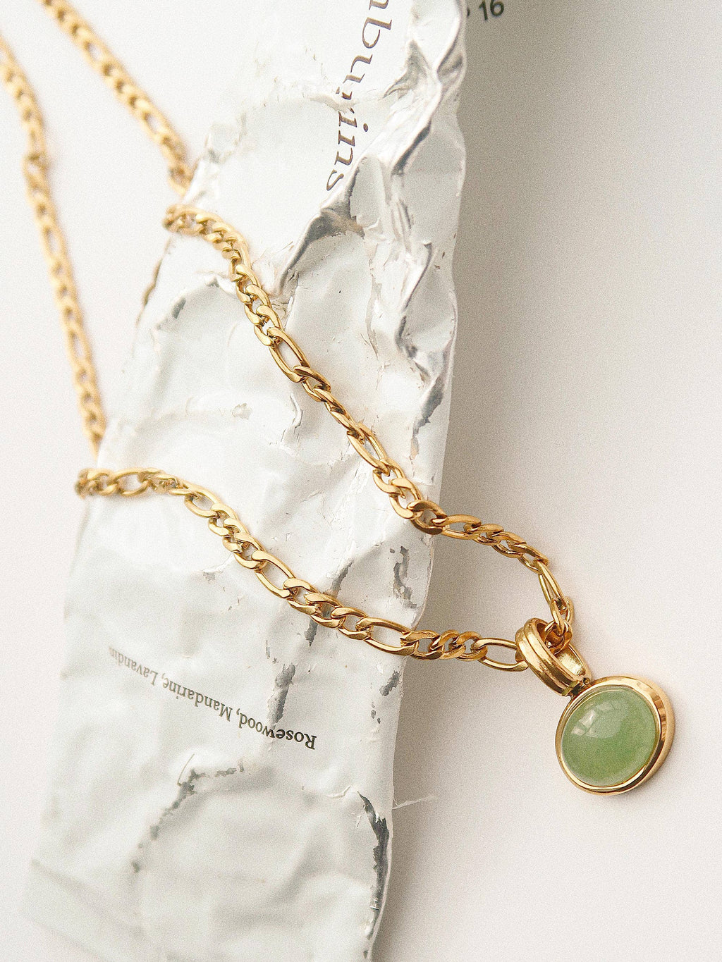 Gold necklace with a green pendant on a marble surface