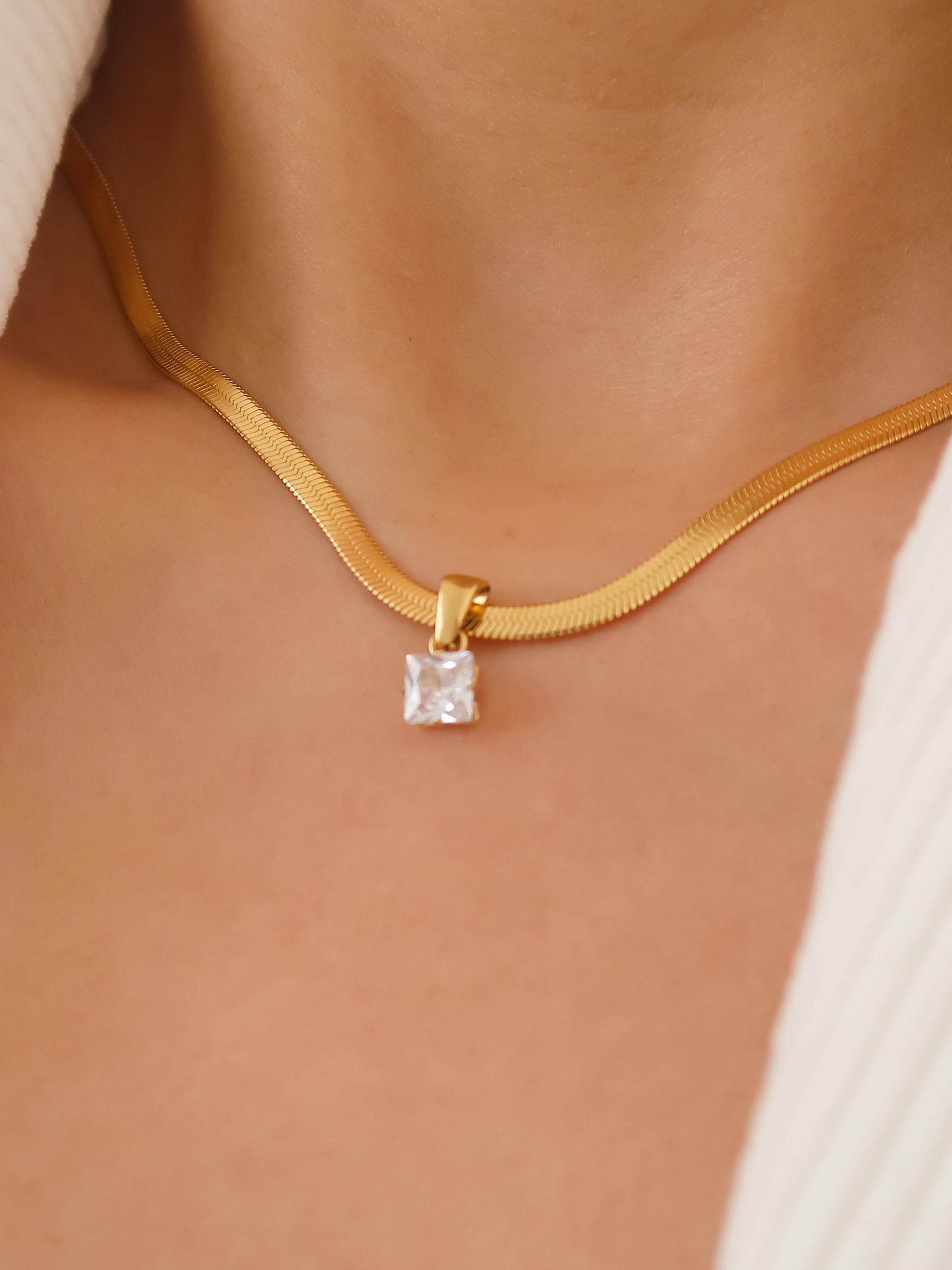 Gold necklace with a square pendant on a person's neck
