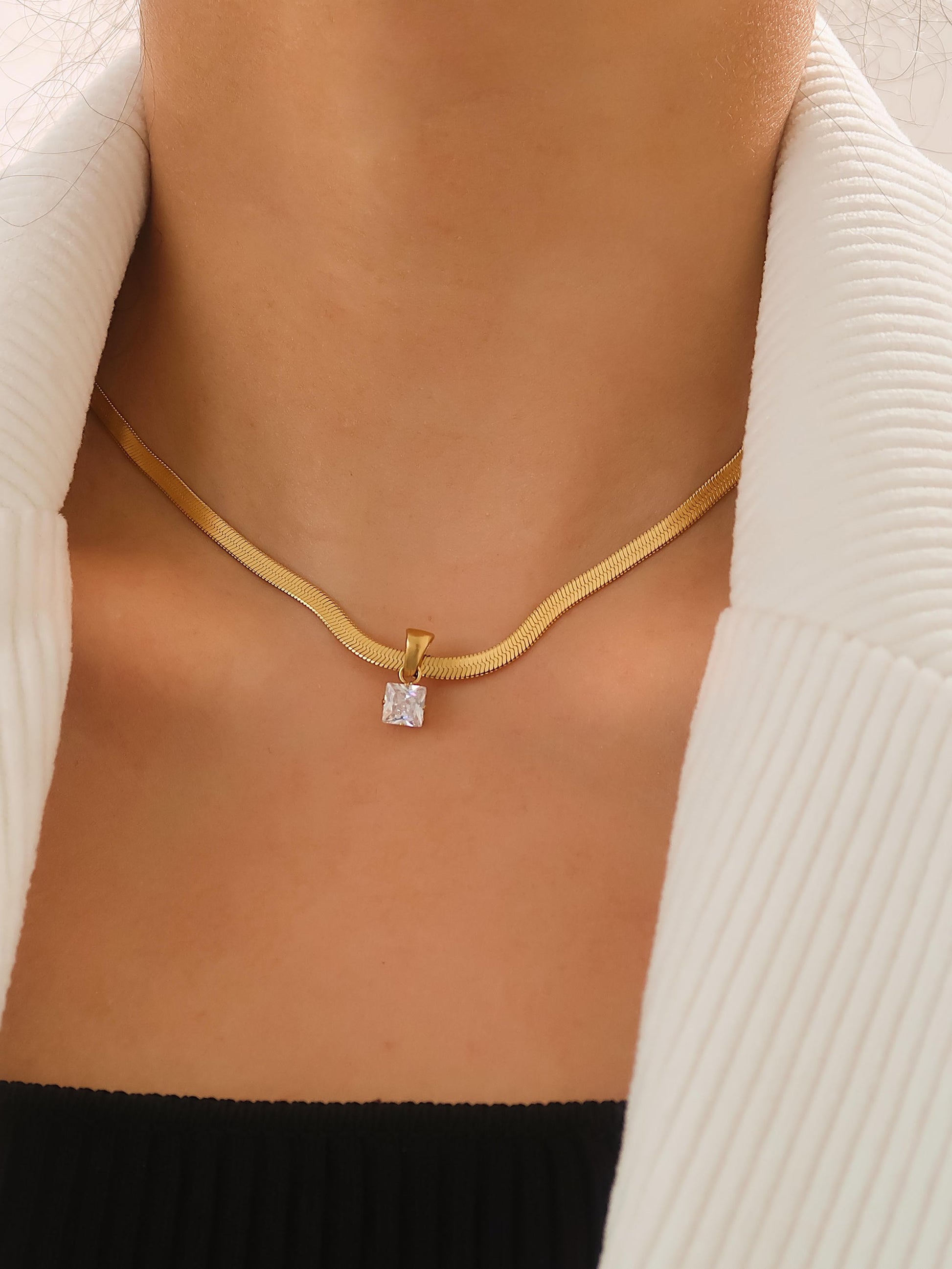 Gold necklace with a diamond pendant on a person wearing a white cardigan.