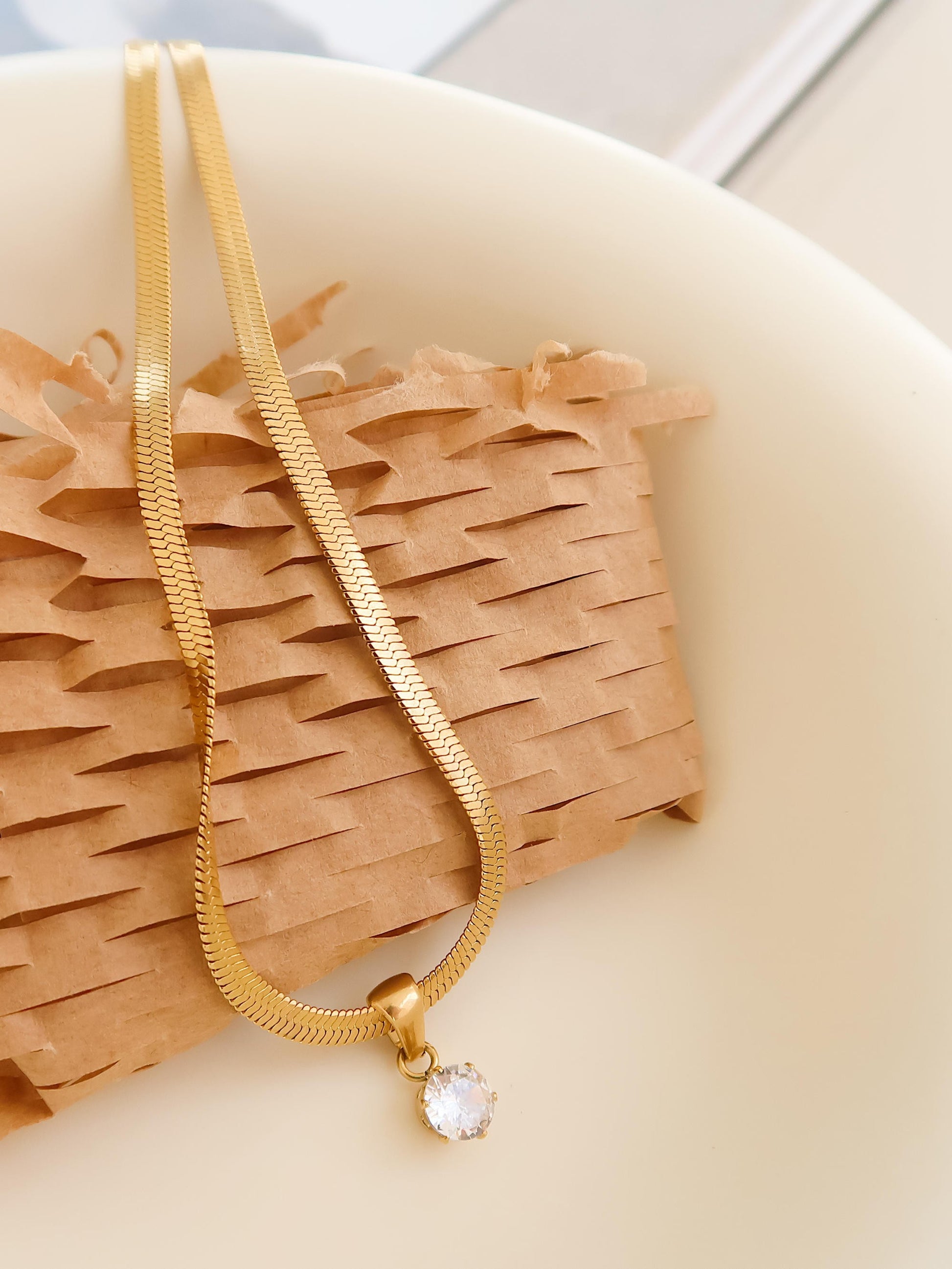 Gold necklace with a pendant on a textured beige surface