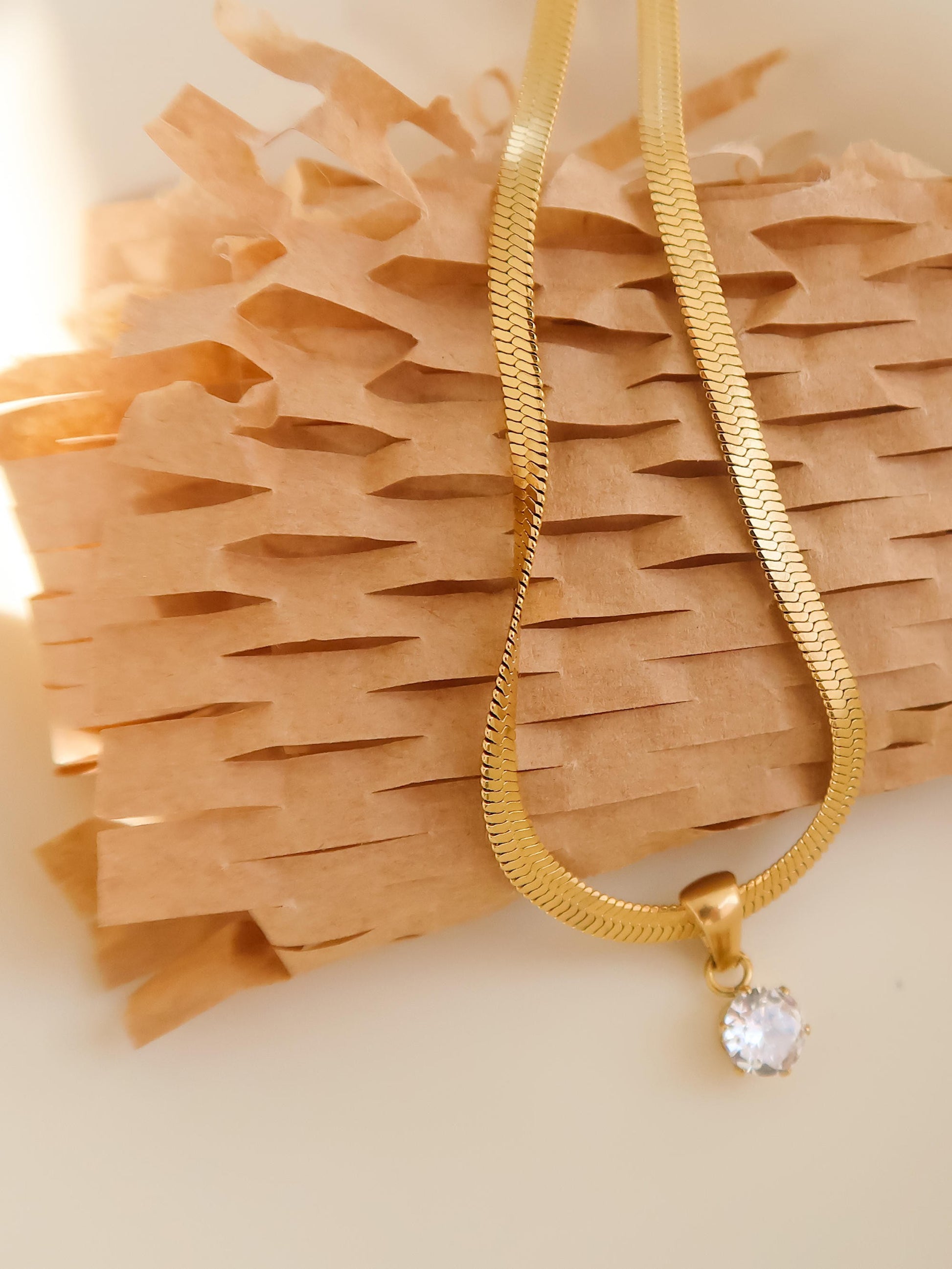 Gold necklace with a clear pendant on a textured beige surface