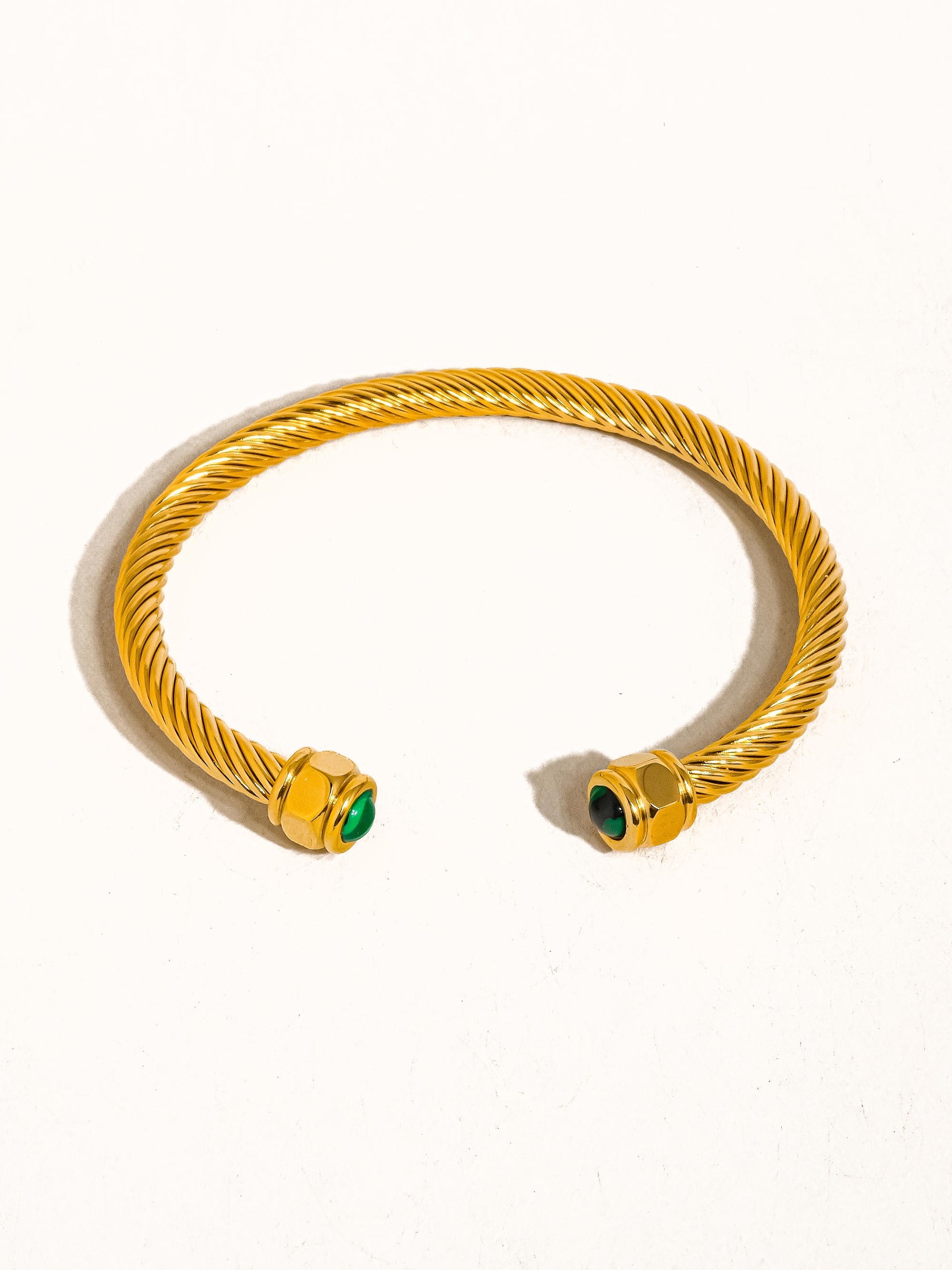 Gold bracelet with green gemstones on a white background