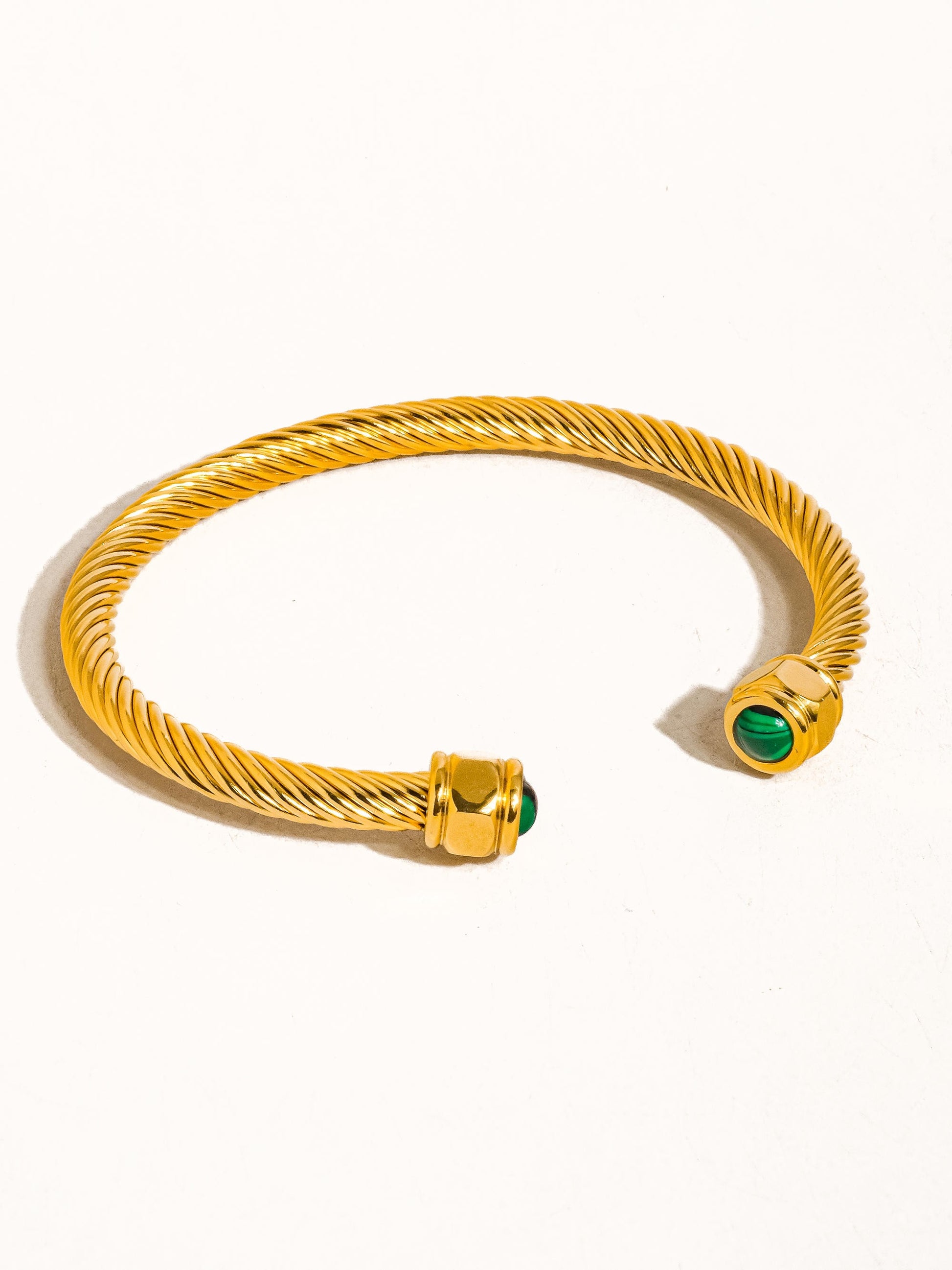 Gold bracelet with green gemstones on a white background