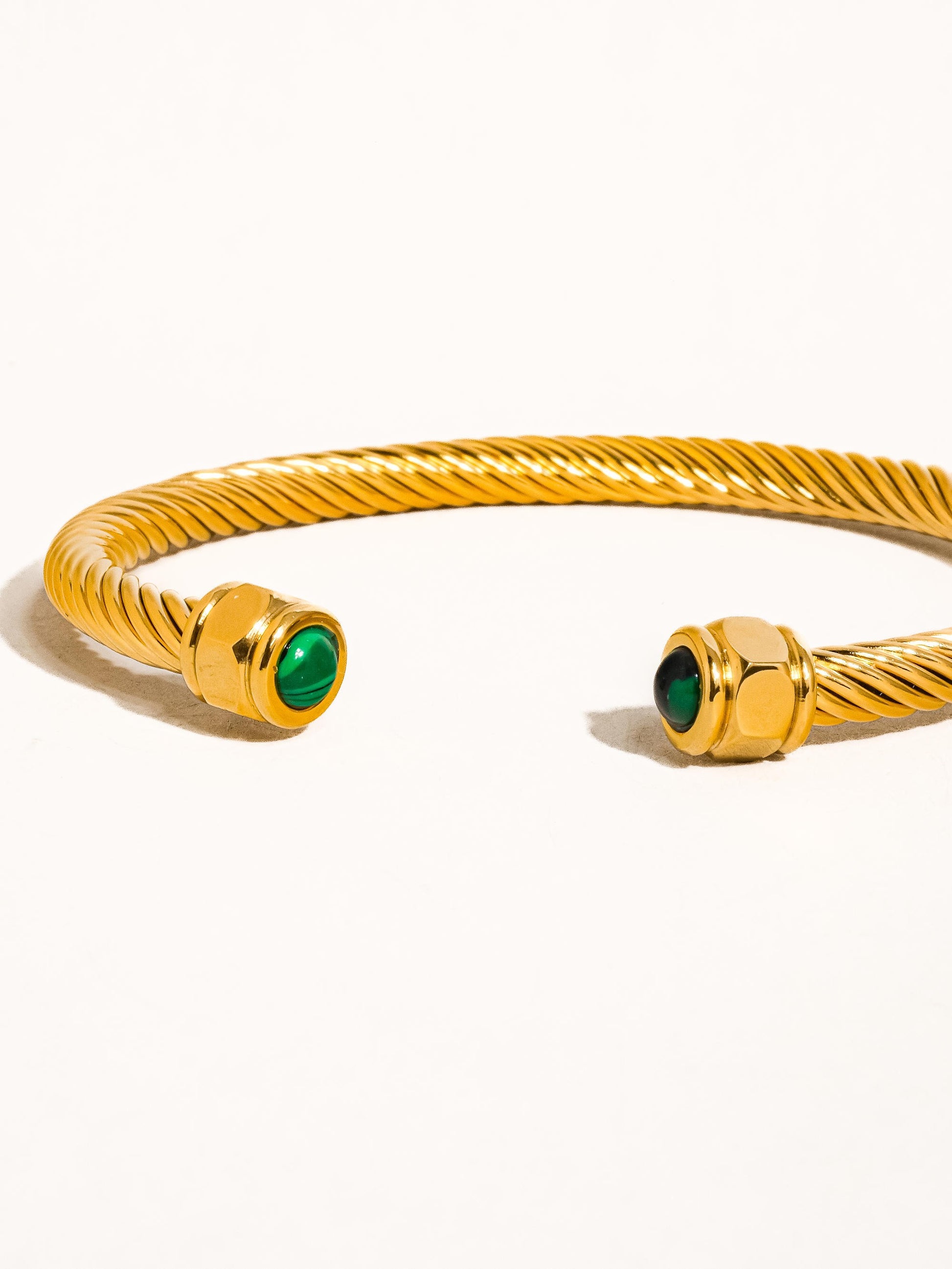 Gold bracelet with green gemstones on a white background