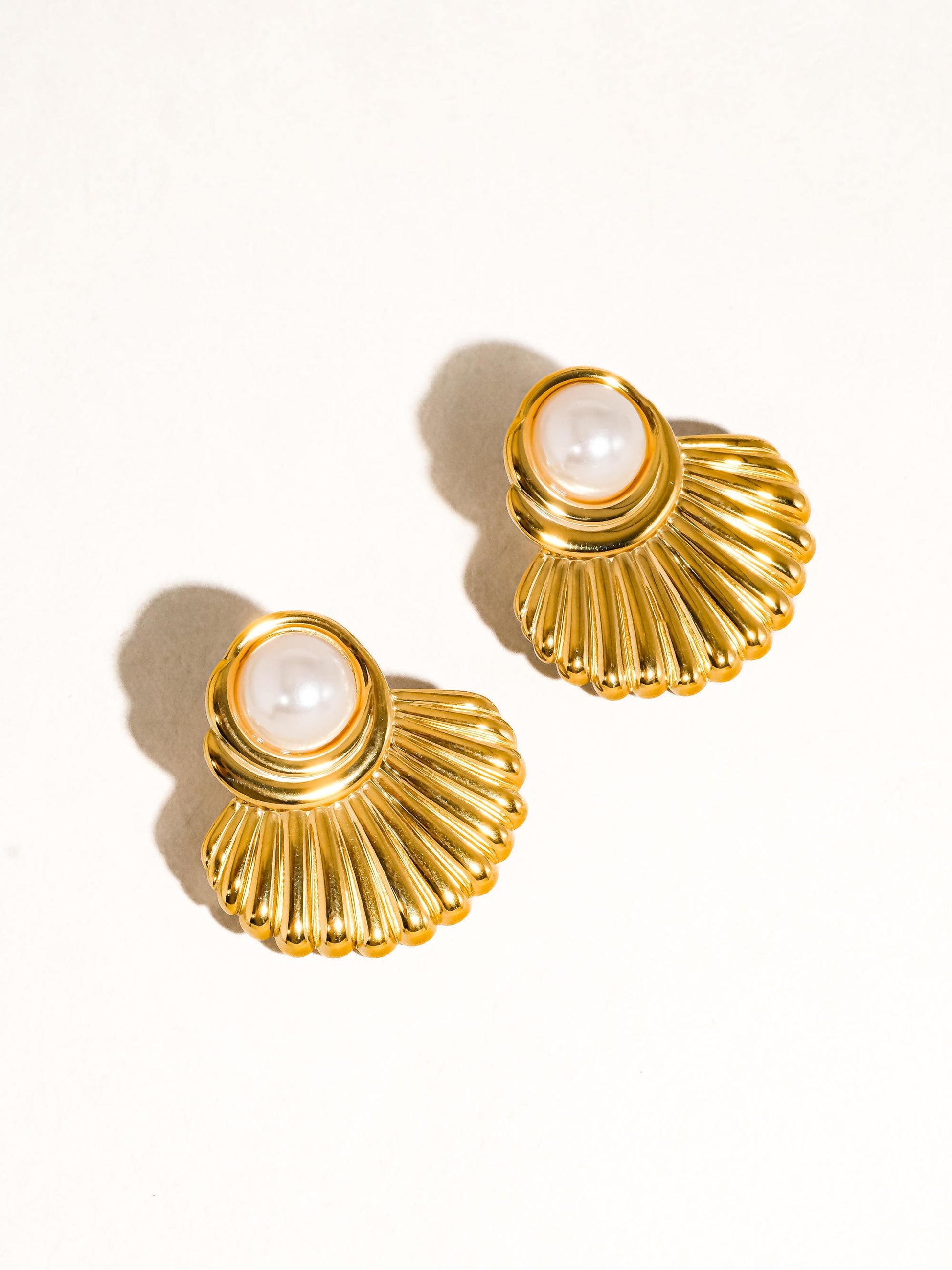 Gold shell-shaped earrings with pearl centers on a white background
