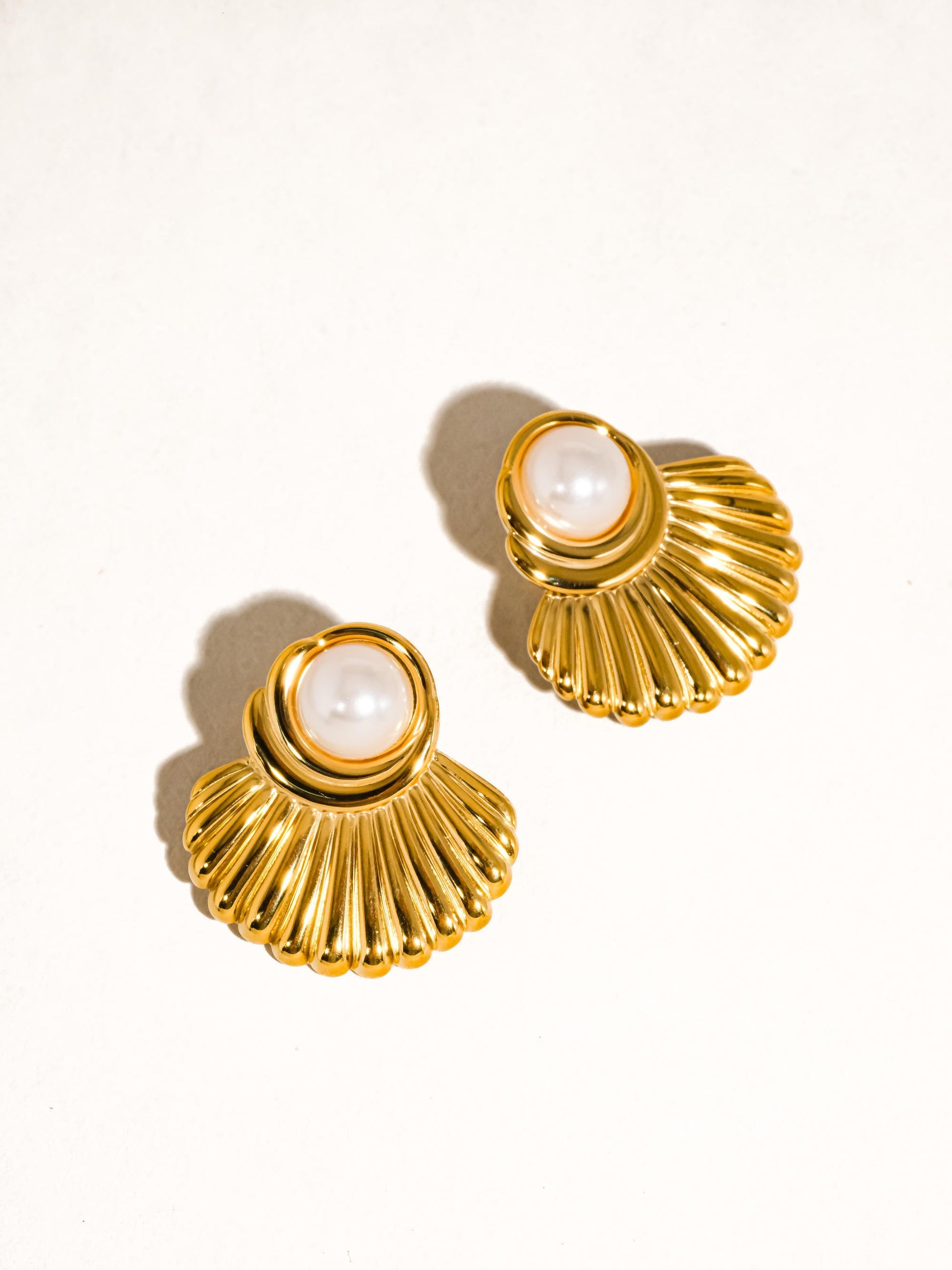 Gold shell-shaped earrings with pearl centers on a white background