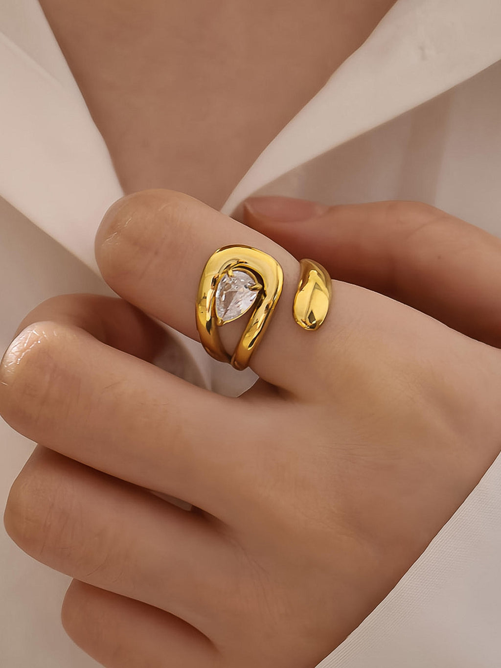 Gold ring with a clear gemstone on a hand against a neutral background