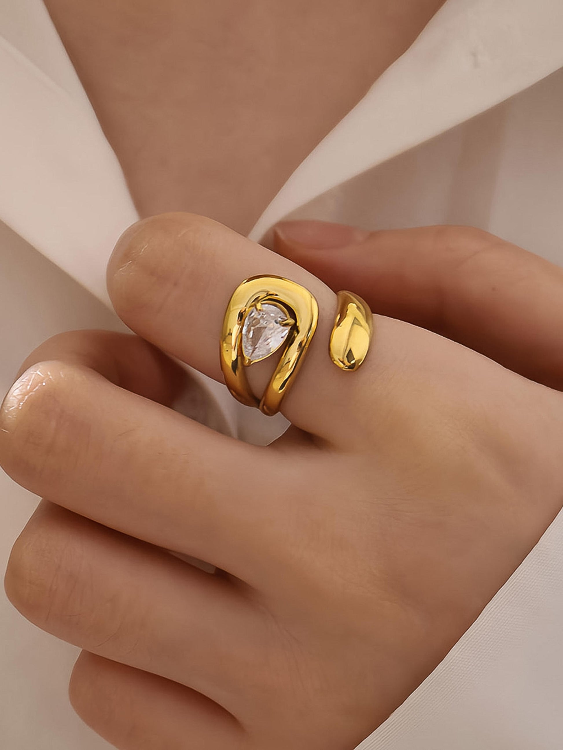 Gold ring with a clear gemstone on a hand against a neutral background