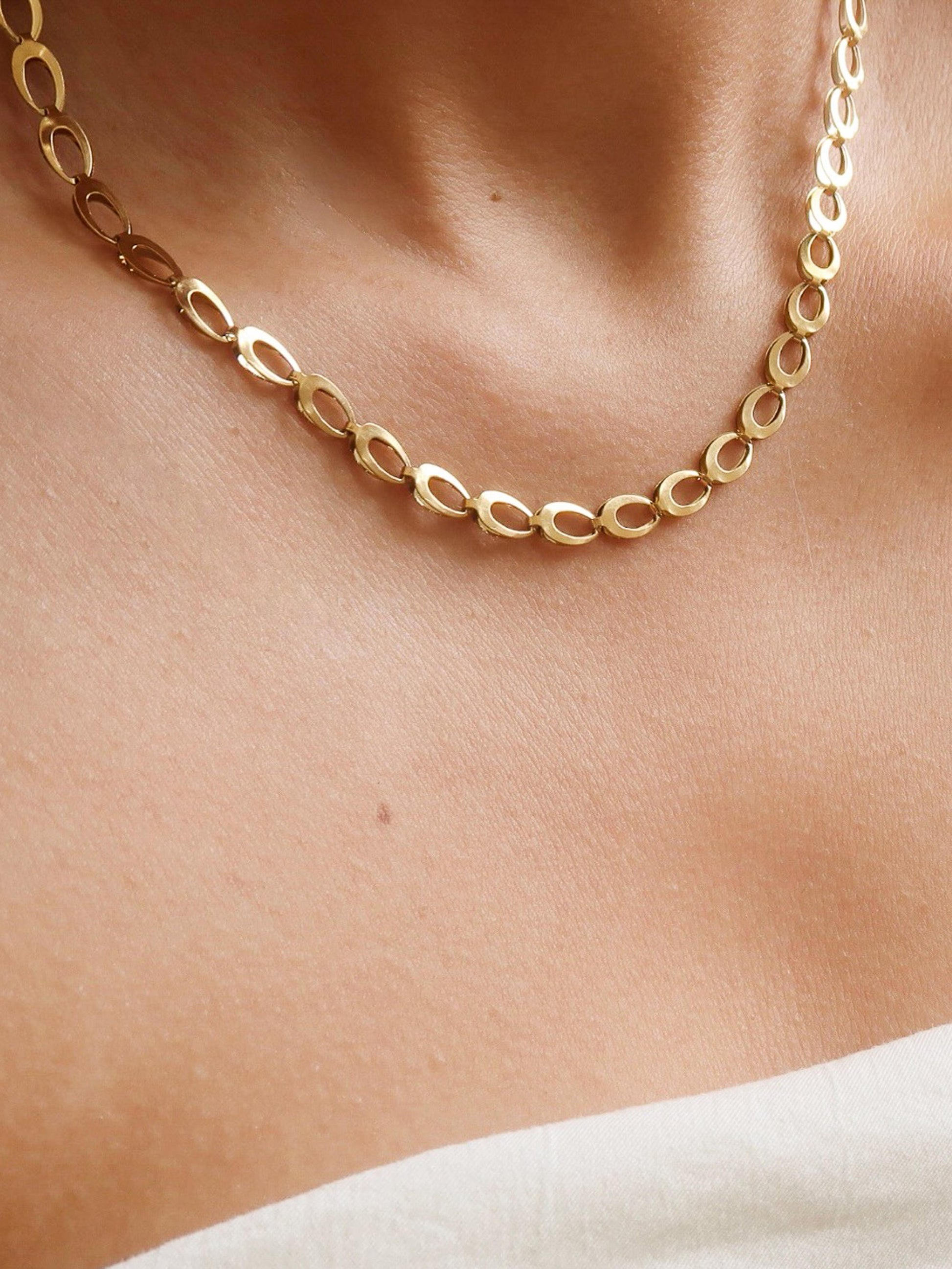 Gold chain necklace on a person's neck with a neutral background