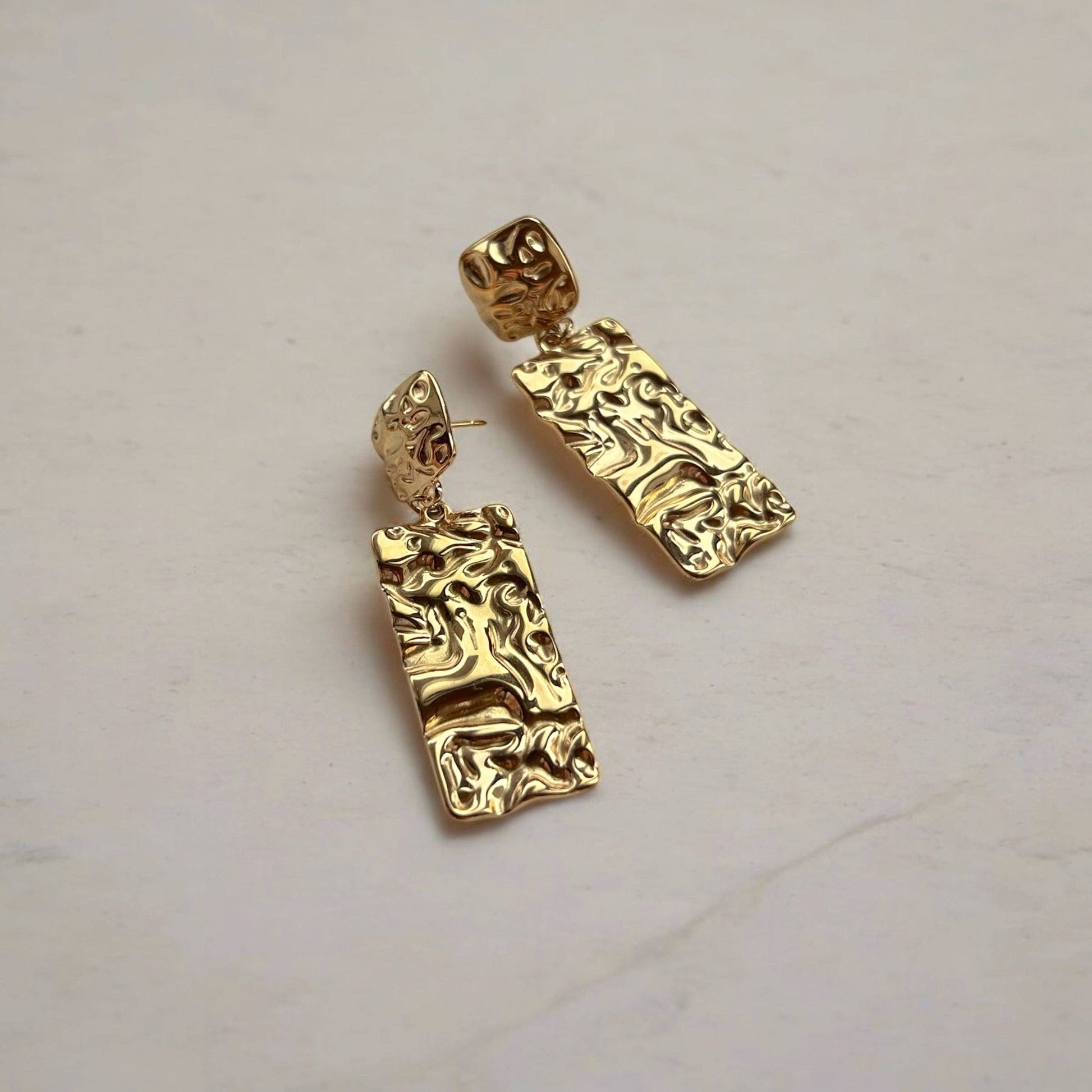 Gold earrings with intricate designs on a light background