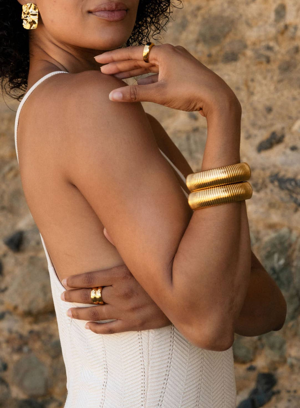 Woman wearing gold jewelry against a natural stone background