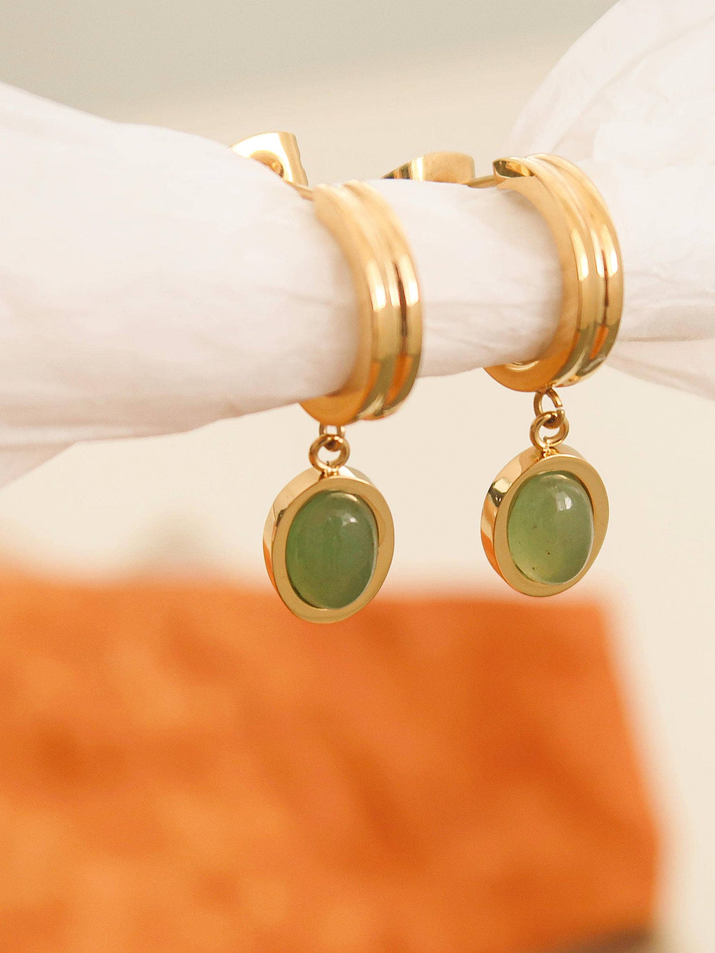 Gold hoop earrings with green stones on a white marble surface.
