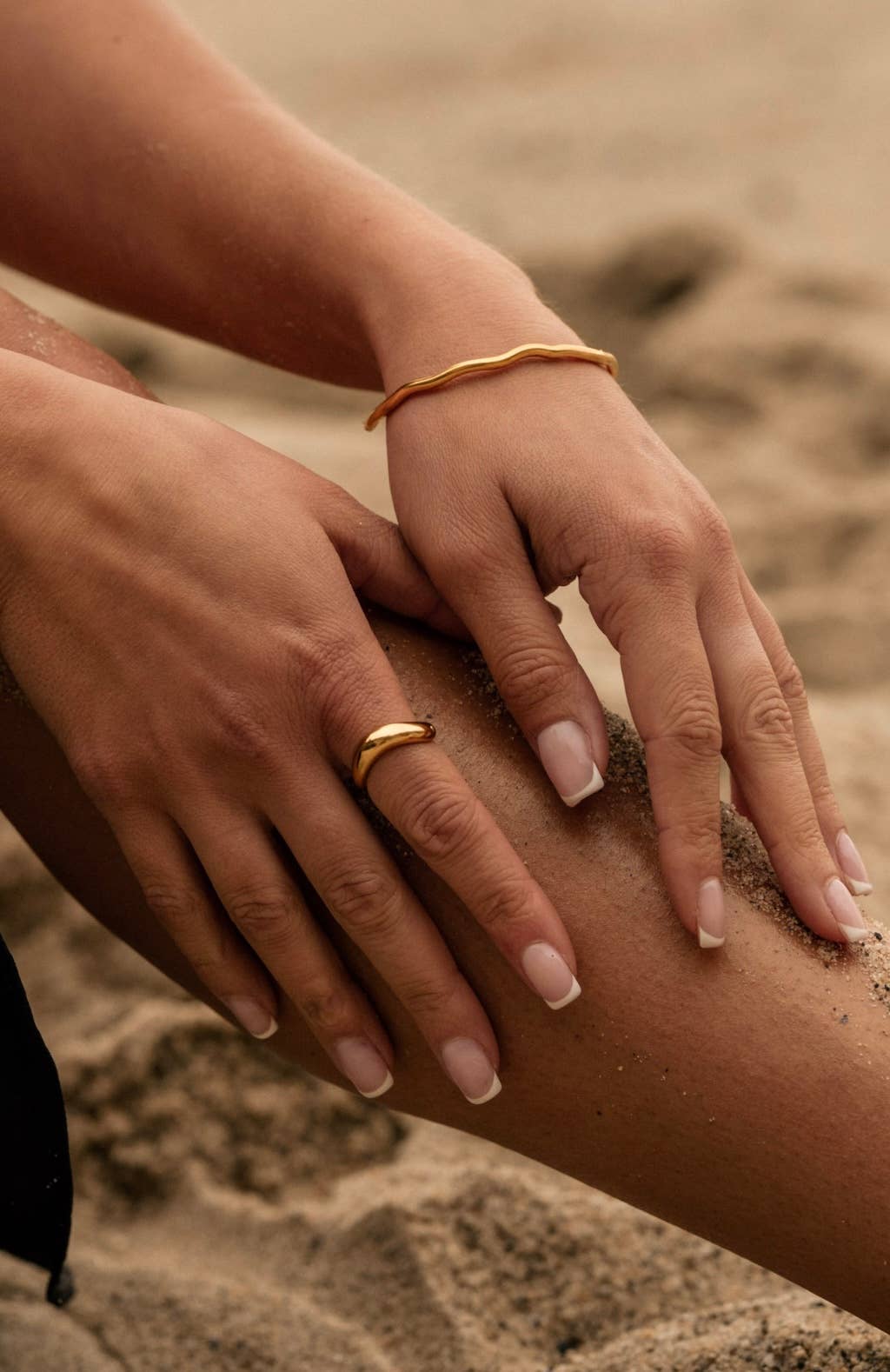Close-up of hands with gold rings and bangles on a sandy background
