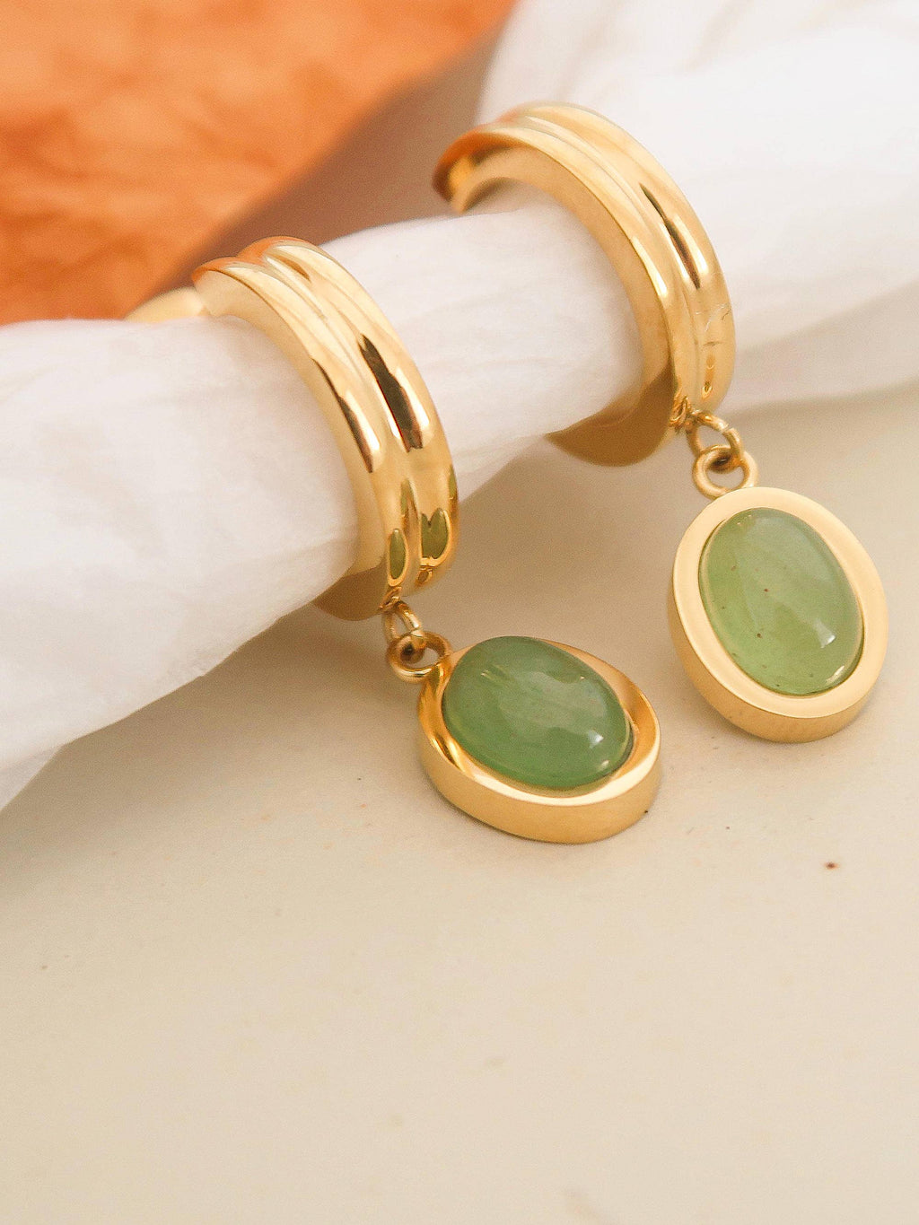 Gold hoop earrings with green stones on a white surface