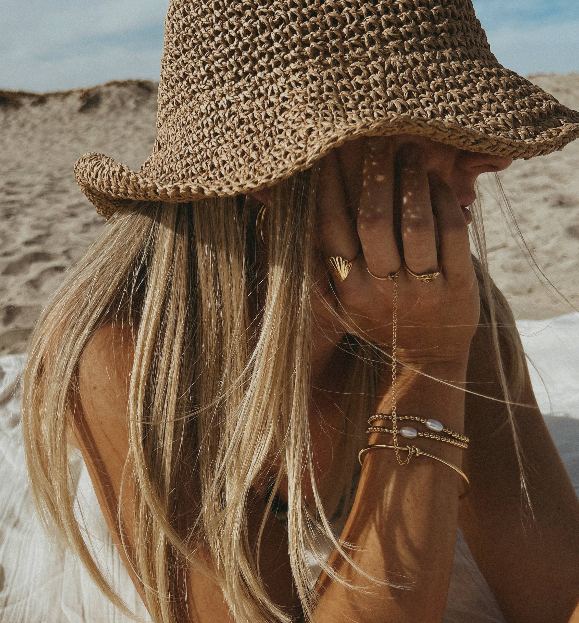 Person wearing a straw hat and gold jewelry on a beach
