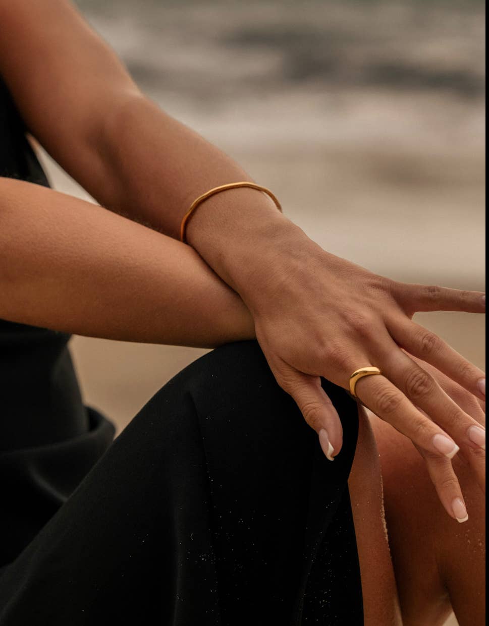 Close-up of a person's hand with a gold ring and bracelet against a blurred natural background