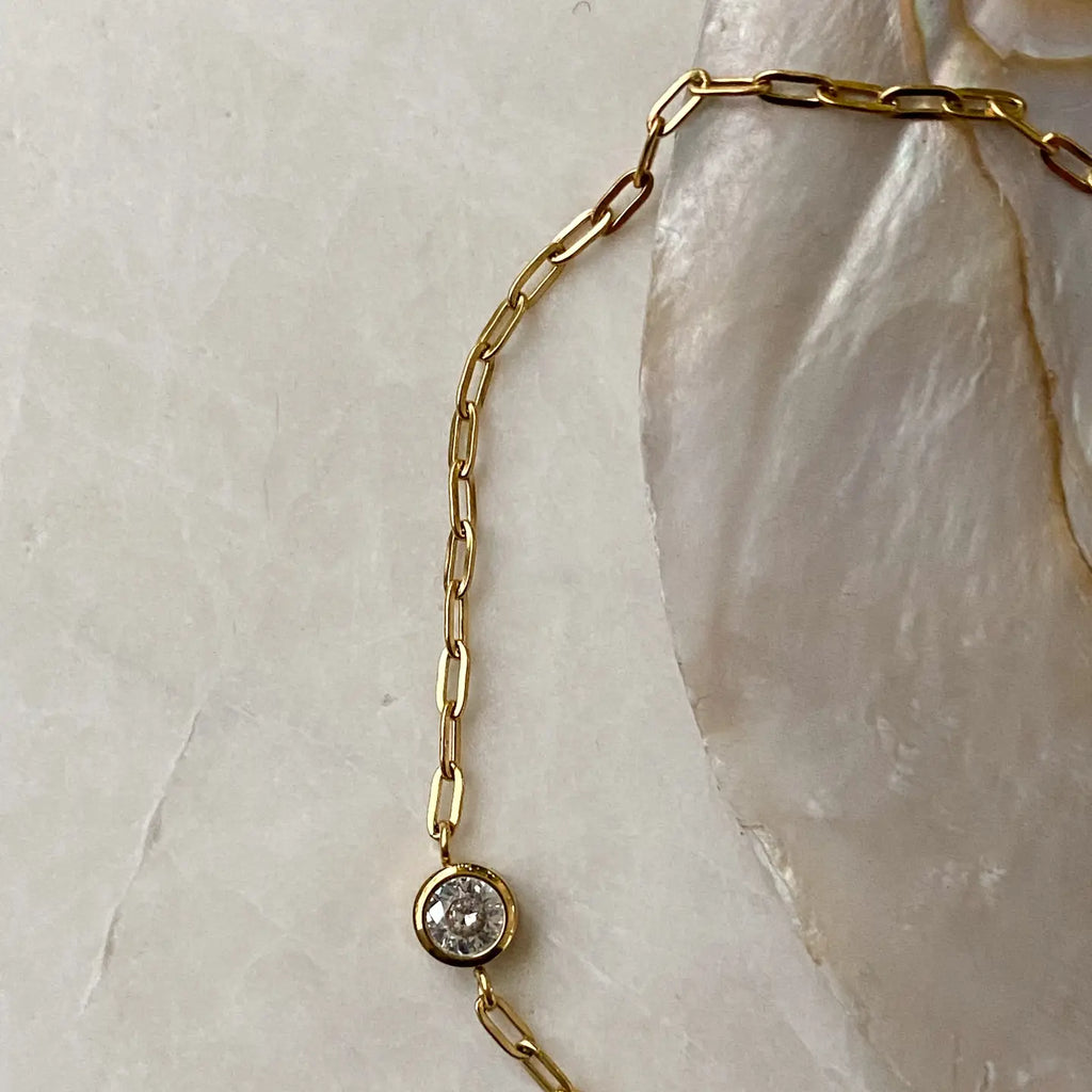 Gold chain necklace with a small round pendant on a light stone background