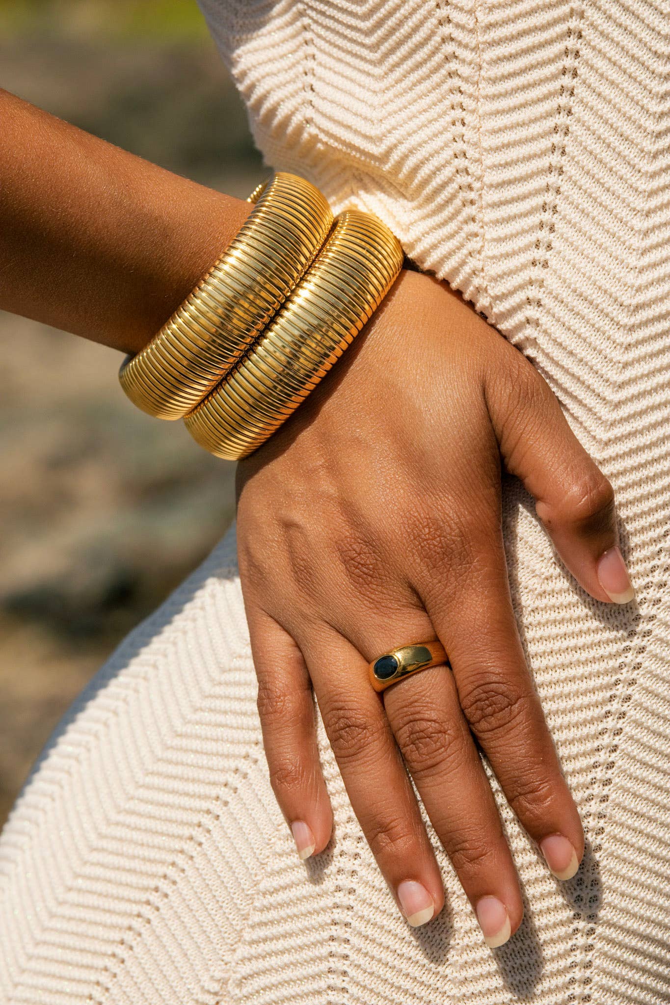 Hand wearing gold bangles and a ring on a textured fabric background