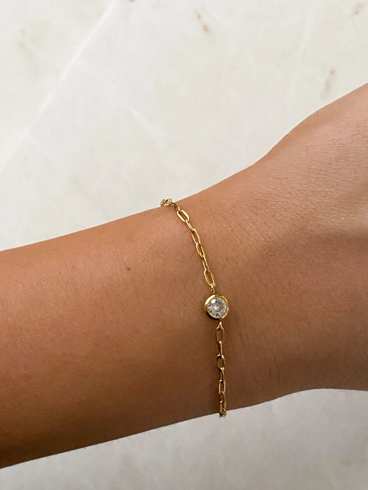 Gold bracelet with a pearl charm on a wrist against a neutral background
