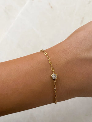 Gold bracelet with a pearl charm on a wrist against a neutral background
