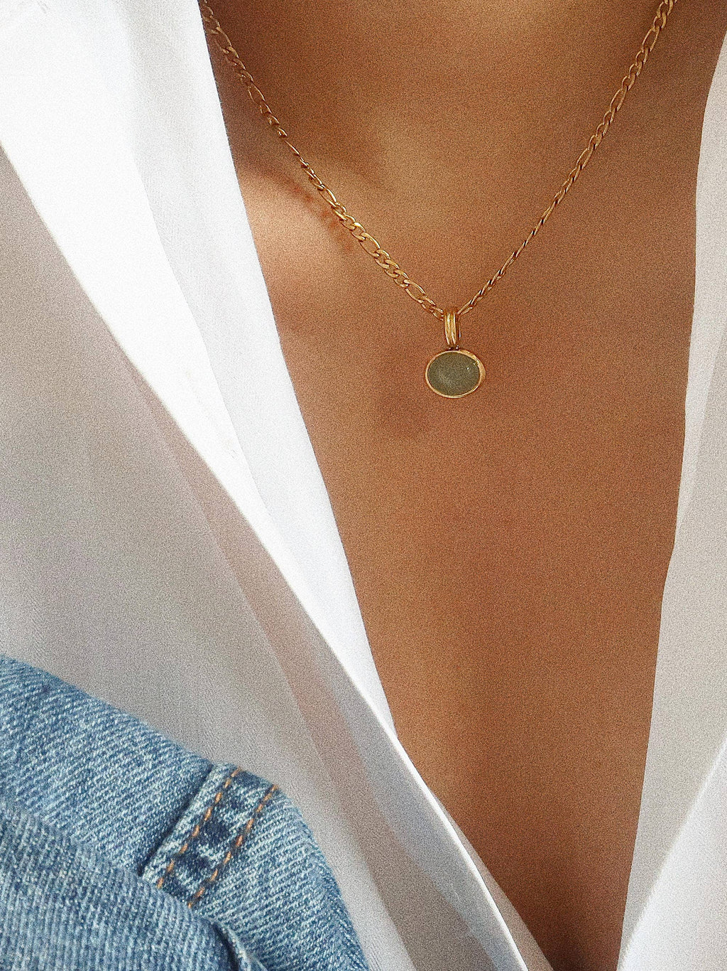 Gold necklace with a green pendant on a person wearing a white shirt and blue jeans.