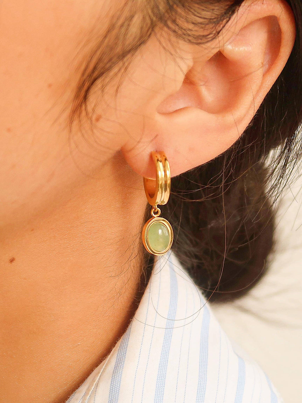 Gold hoop earring with a green gemstone worn by a person.