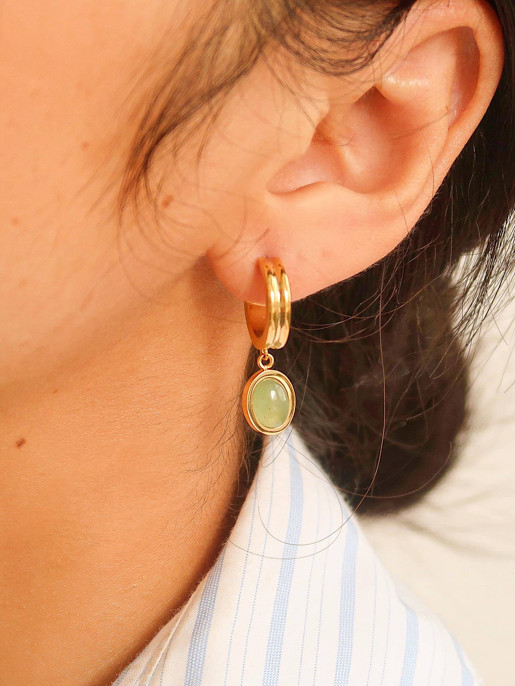 Gold hoop earring with a green gemstone worn by a person.