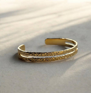 Gold bracelet with textured design on a light background