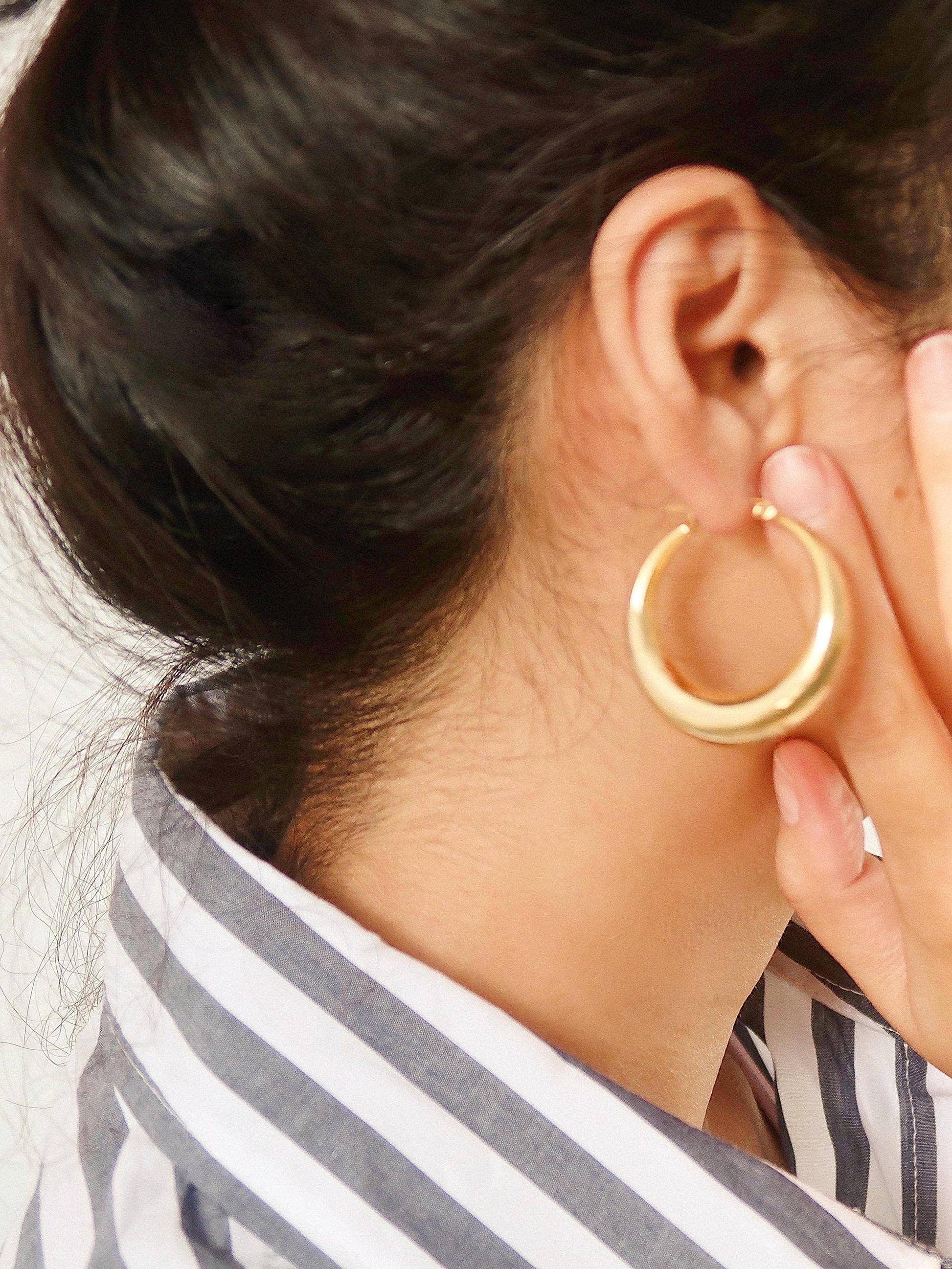 Gold hoop earring worn by a person with dark hair and a striped garment.